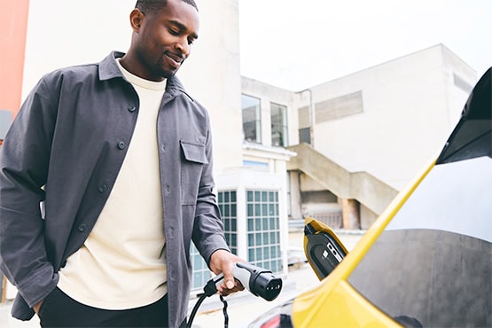Man plugging in his electric vehicle with city buildings in the background